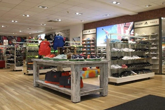 Ein gut beleuchteter Sportladen präsentiert eine breite Auswahl an Sportschuhen und Taschen auf Holzregalen.