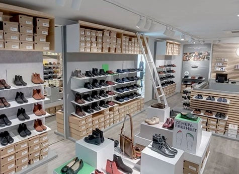 Innenansicht eines modernen Schuhgeschäfts mit Regalen voller Schuhe und Leitern zum Erreichen höherer Ebenen