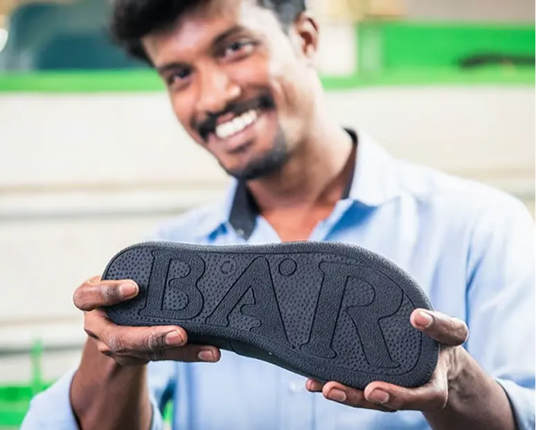 Ein Mann in einem blauen Hemd hält eine Schuhsohle mit dem Schriftzug BAR in die Kamera