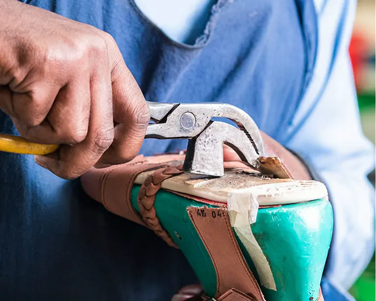 Nahaufnahme eines Handwerkers, der mit einem Hammer an einem Schuhmodell arbeitet