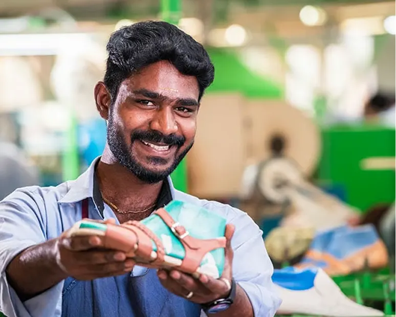 Ein lächelnder Mann in einer Fabrik zeigt stolz einen hergestellten Schuh.