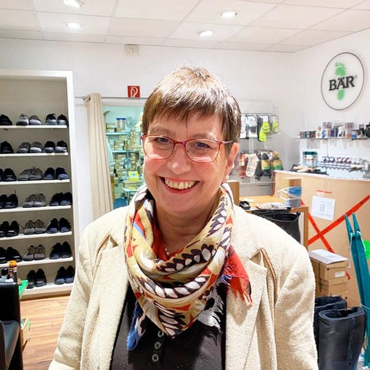 Eine lächelnde Frau mit Brille und buntem Schal in einem Schuhgeschäft