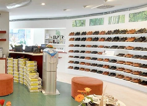 Innenansicht eines Schuhgeschäfts mit Regalen voller Herrenschuhe und einer gemütlichen Sitzecke